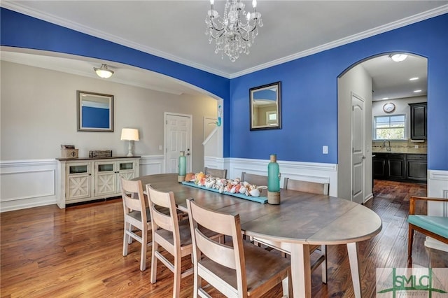 dining room with ornamental molding, arched walkways, a wainscoted wall, and wood finished floors