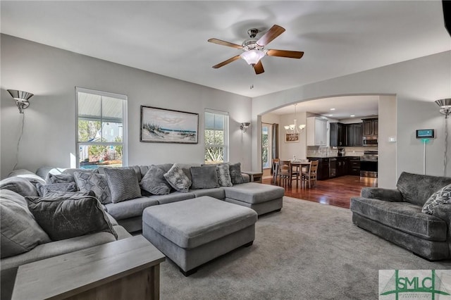 living area with arched walkways, ceiling fan with notable chandelier, dark wood-style floors, and a wealth of natural light