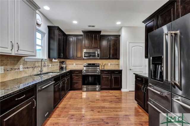 kitchen featuring a sink, visible vents, appliances with stainless steel finishes, light wood-type flooring, and dark stone countertops