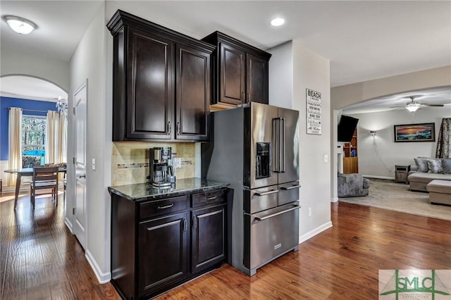 kitchen with arched walkways, high end refrigerator, open floor plan, decorative backsplash, and hardwood / wood-style floors