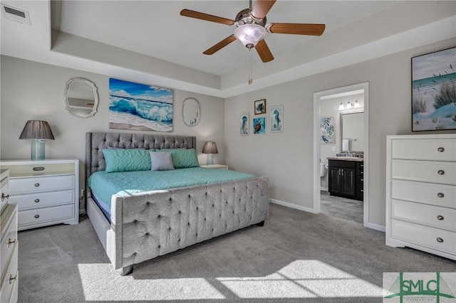 bedroom featuring a raised ceiling, visible vents, light carpet, ensuite bath, and baseboards