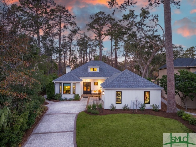 view of front of property featuring driveway, a front lawn, roof with shingles, and a chimney