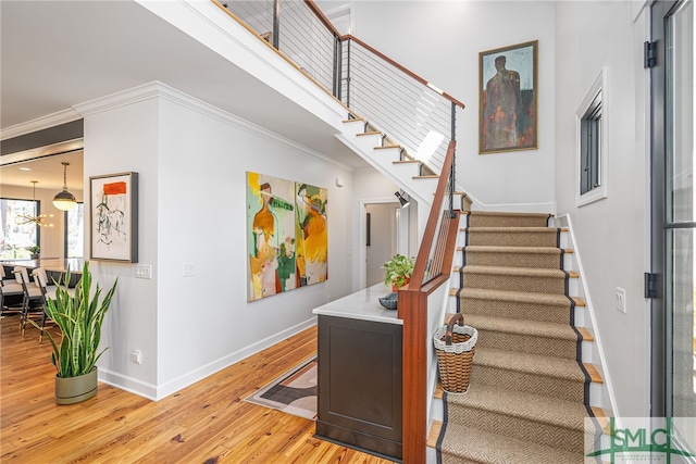 stairs with baseboards, wood finished floors, an inviting chandelier, a high ceiling, and crown molding