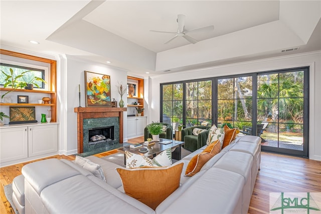 living room with light wood finished floors, a fireplace, visible vents, and a raised ceiling