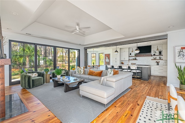 living area featuring light wood-type flooring, visible vents, a raised ceiling, and crown molding