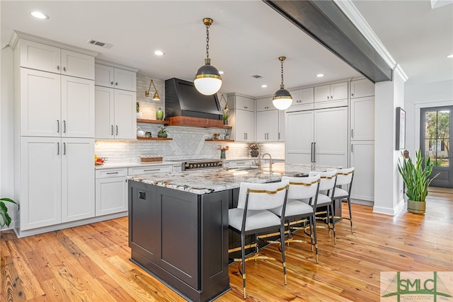 kitchen with visible vents, high quality appliances, custom exhaust hood, light wood-style floors, and open shelves