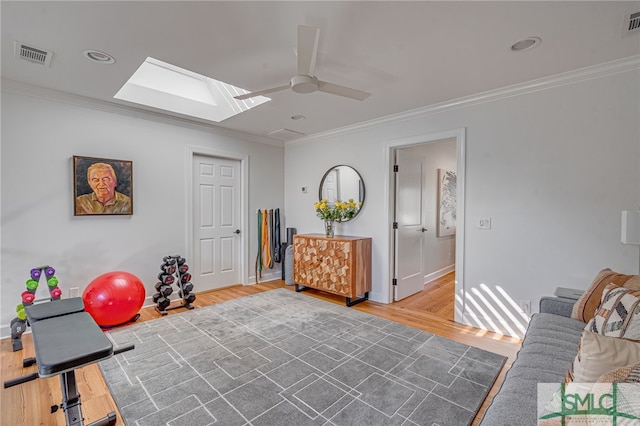 exercise room featuring ceiling fan, a skylight, wood finished floors, visible vents, and ornamental molding