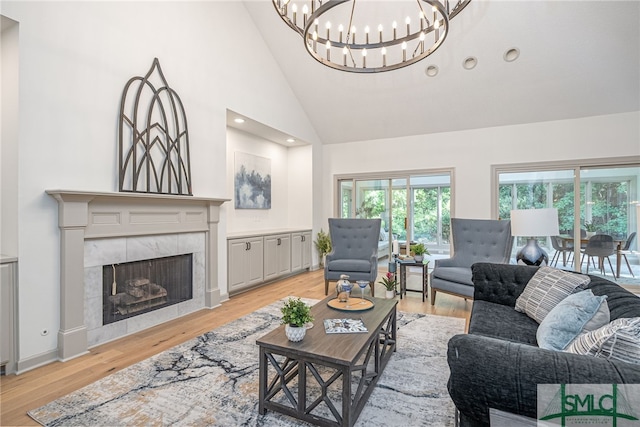 living area featuring baseboards, a tile fireplace, light wood-style flooring, an inviting chandelier, and high vaulted ceiling