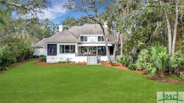 back of house featuring a balcony, a sunroom, a yard, roof with shingles, and a chimney