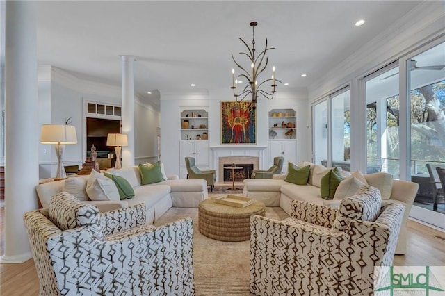 living room featuring a glass covered fireplace, light wood-style flooring, crown molding, built in shelves, and recessed lighting