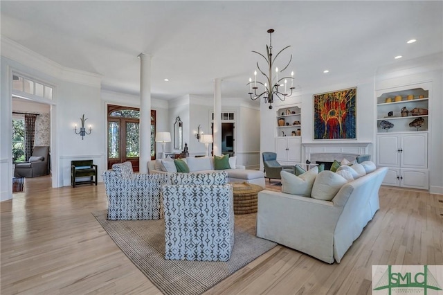 living area featuring light wood finished floors, decorative columns, built in features, crown molding, and a fireplace