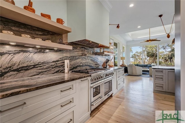 kitchen featuring range with two ovens, premium range hood, open shelves, tasteful backsplash, and a raised ceiling