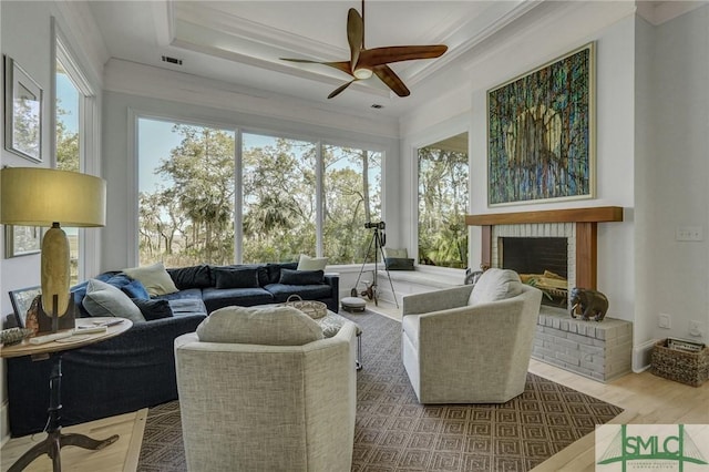 sunroom featuring visible vents, a tray ceiling, a brick fireplace, and a ceiling fan