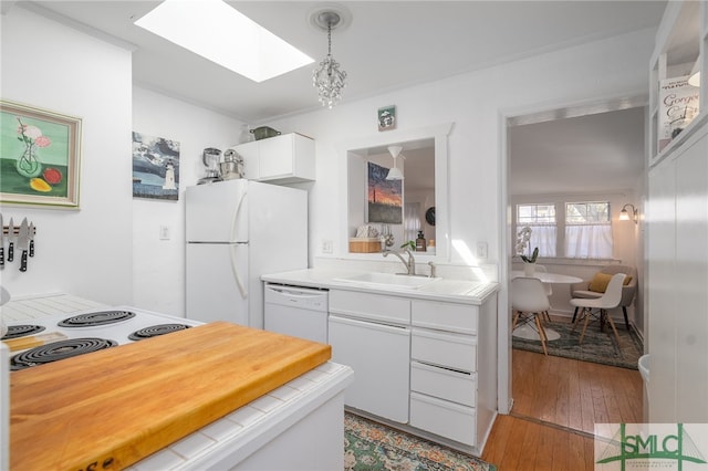 kitchen with white appliances, a skylight, a sink, white cabinets, and tile counters