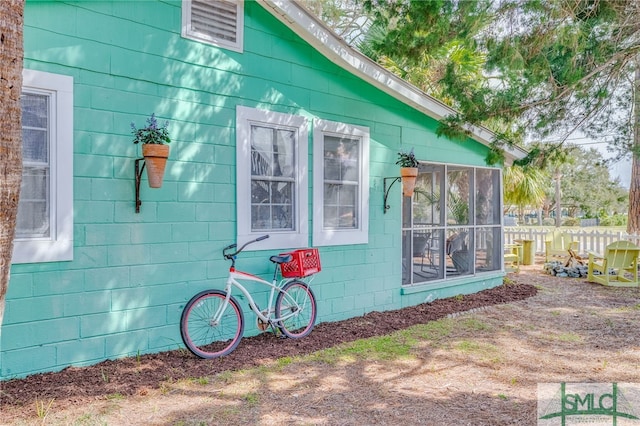 view of home's exterior with a sunroom, concrete block siding, and fence