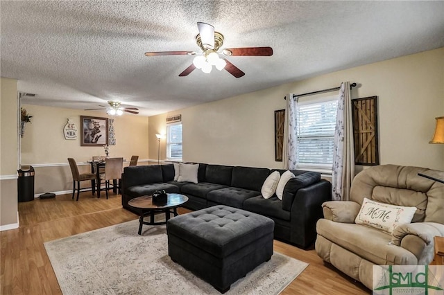 living room with a ceiling fan, baseboards, a textured ceiling, and light wood finished floors