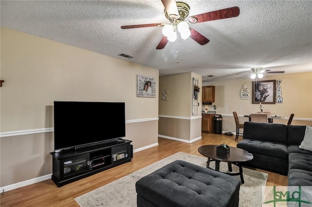 living area featuring light wood finished floors, baseboards, visible vents, and a textured ceiling