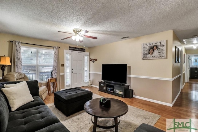 living area featuring visible vents, light wood-style flooring, attic access, ceiling fan, and baseboards