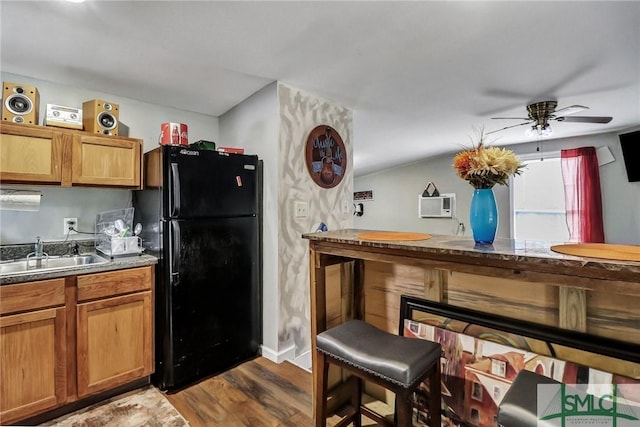 kitchen with a sink, a ceiling fan, freestanding refrigerator, brown cabinets, and dark wood-style floors