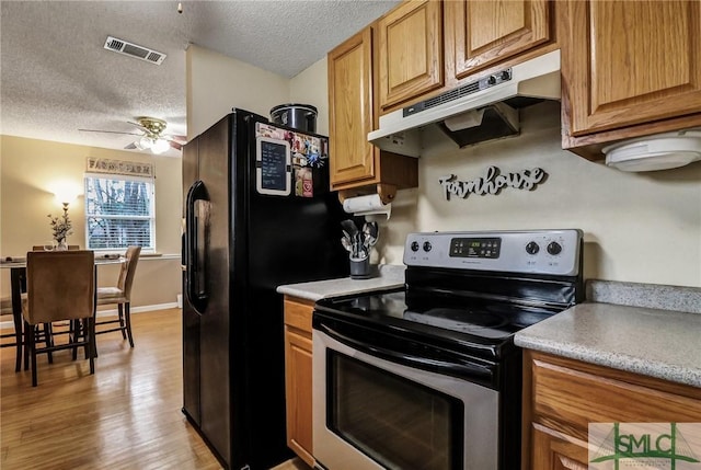 kitchen featuring visible vents, black refrigerator with ice dispenser, a ceiling fan, under cabinet range hood, and stainless steel electric range