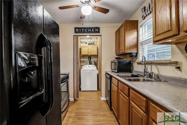 kitchen featuring washer / dryer, light wood-style floors, brown cabinets, black appliances, and a sink