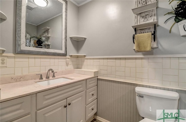 half bathroom featuring wainscoting, crown molding, vanity, and toilet