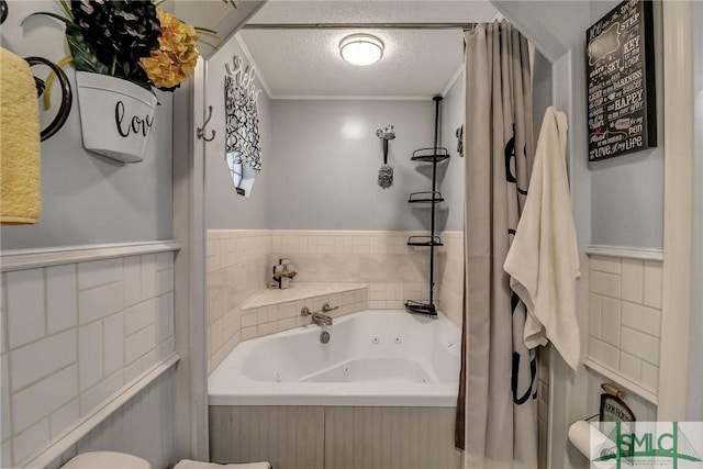 bathroom featuring a textured ceiling, a jetted tub, wainscoting, and tile walls