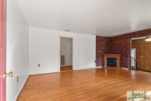 unfurnished living room with a brick fireplace, visible vents, and light wood finished floors