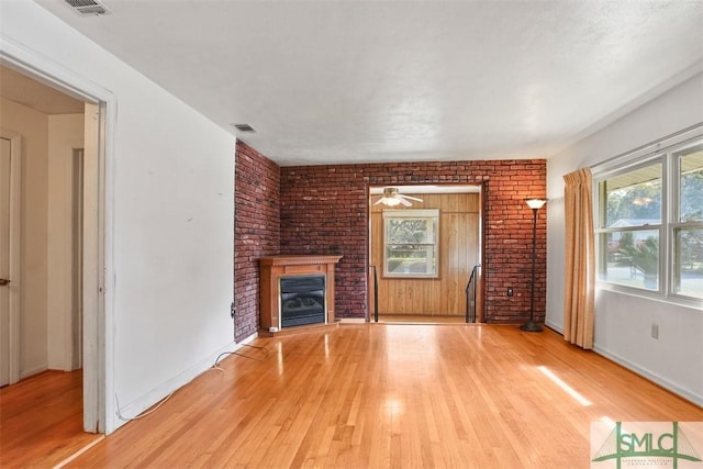 unfurnished living room with light wood-style flooring, a brick fireplace, visible vents, and baseboards