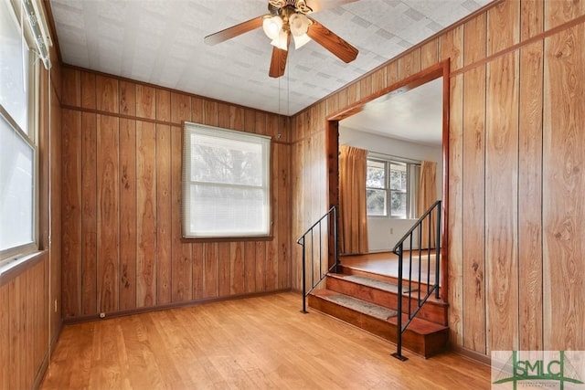 unfurnished room featuring wood walls, ceiling fan, stairs, and wood finished floors