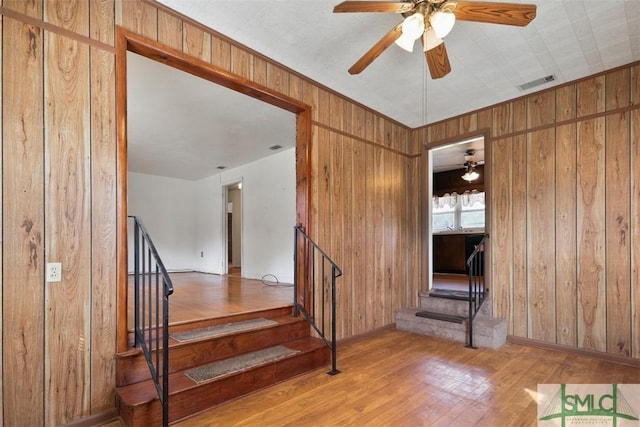 stairs featuring visible vents, baseboards, ceiling fan, wood finished floors, and wood walls