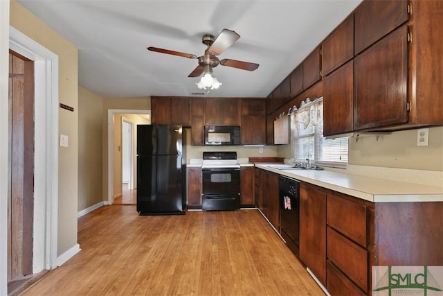 kitchen featuring baseboards, light wood-style floors, light countertops, black appliances, and a sink