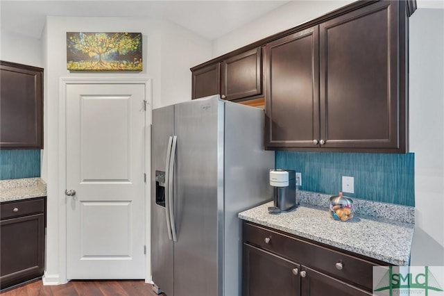 kitchen with tasteful backsplash, dark wood-type flooring, dark brown cabinets, light stone countertops, and stainless steel fridge