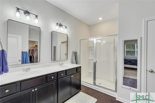 ensuite bathroom with double vanity, a shower stall, a sink, and wood finished floors