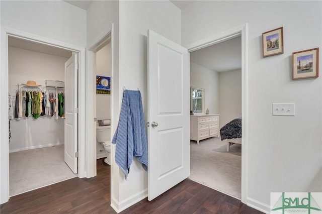 ensuite bathroom featuring a walk in closet, toilet, ensuite bath, wood finished floors, and baseboards