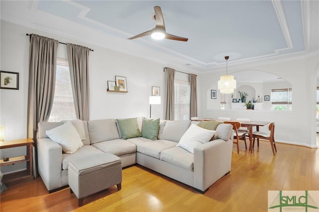 living room with a tray ceiling, arched walkways, light wood-style floors, ornamental molding, and ceiling fan