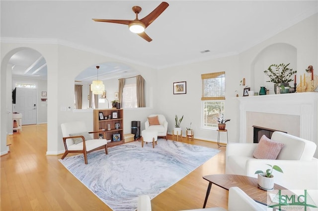 sitting room with ornamental molding, light wood-type flooring, a fireplace, and arched walkways