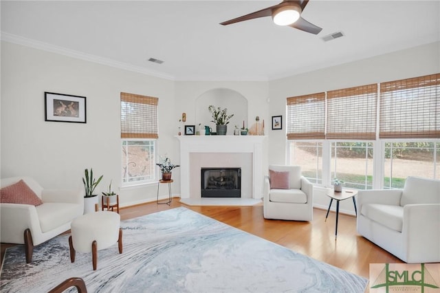 interior space featuring a fireplace with raised hearth, wood finished floors, visible vents, and crown molding