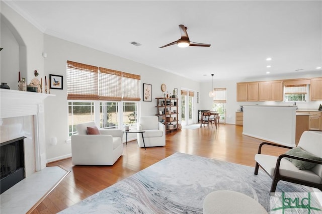 living room featuring light wood finished floors, baseboards, a ceiling fan, a fireplace, and recessed lighting