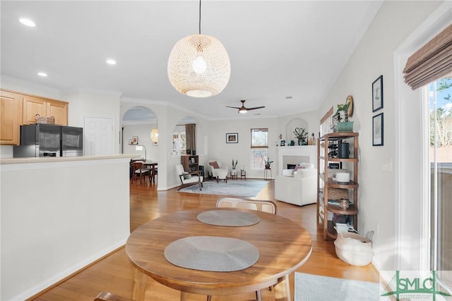 dining area featuring arched walkways, recessed lighting, a fireplace, ornamental molding, and light wood-type flooring