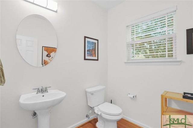 half bathroom with wood finished floors, toilet, and baseboards