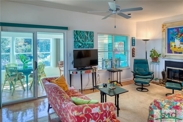 living room featuring a healthy amount of sunlight, baseboards, a ceiling fan, and a glass covered fireplace