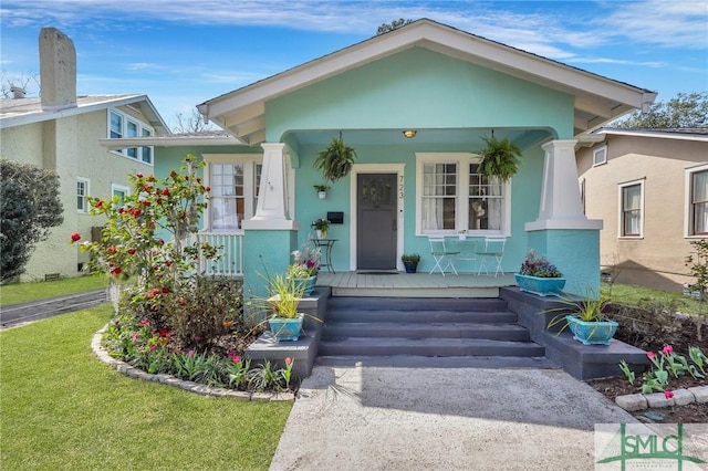 view of front of property with covered porch, a front lawn, and stucco siding