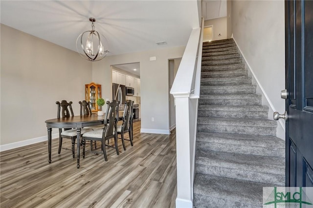 stairs featuring a chandelier, visible vents, baseboards, and wood finished floors