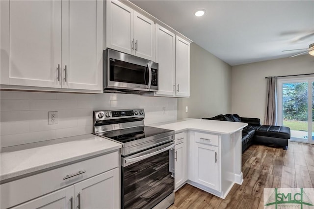 kitchen featuring stainless steel appliances, light countertops, light wood-style flooring, open floor plan, and a peninsula