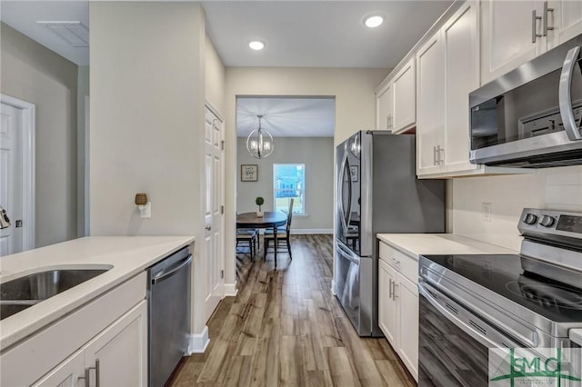 kitchen with appliances with stainless steel finishes, light countertops, white cabinets, and wood finished floors