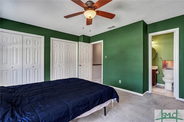 bedroom with multiple closets, carpet flooring, visible vents, and a textured ceiling