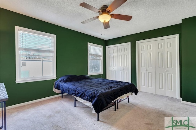 bedroom with a textured ceiling, carpet, two closets, and baseboards