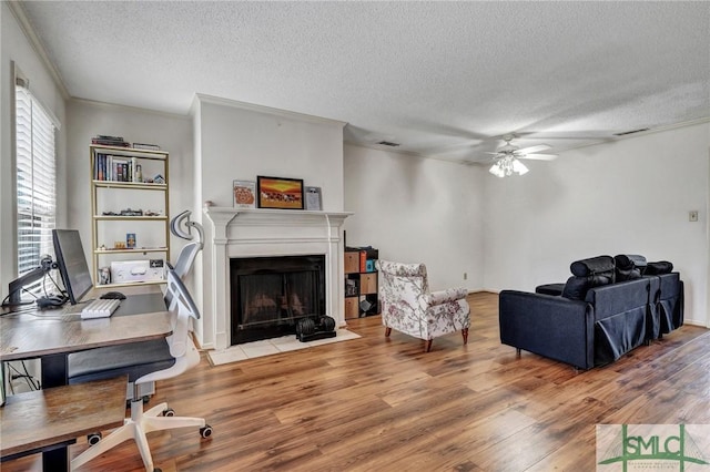 living room with visible vents, a fireplace with flush hearth, a ceiling fan, a textured ceiling, and wood finished floors