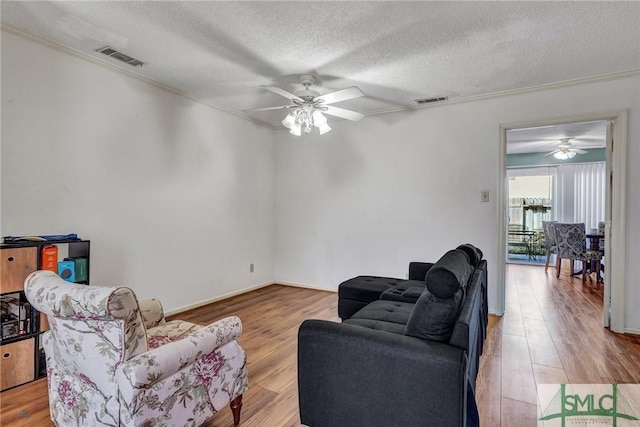 living area featuring a ceiling fan, visible vents, a textured ceiling, and wood finished floors